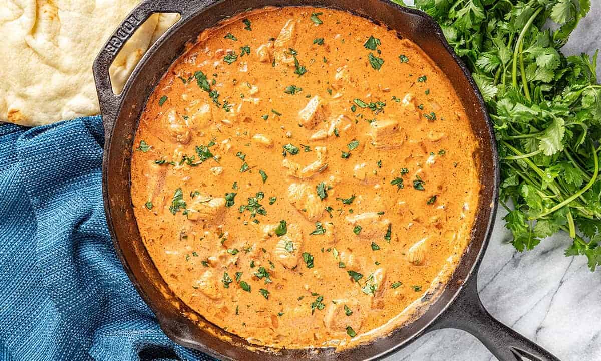 Butter chicken and sauce in skillet with parsley