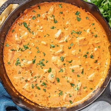 Butter chicken and sauce in skillet with parsley
