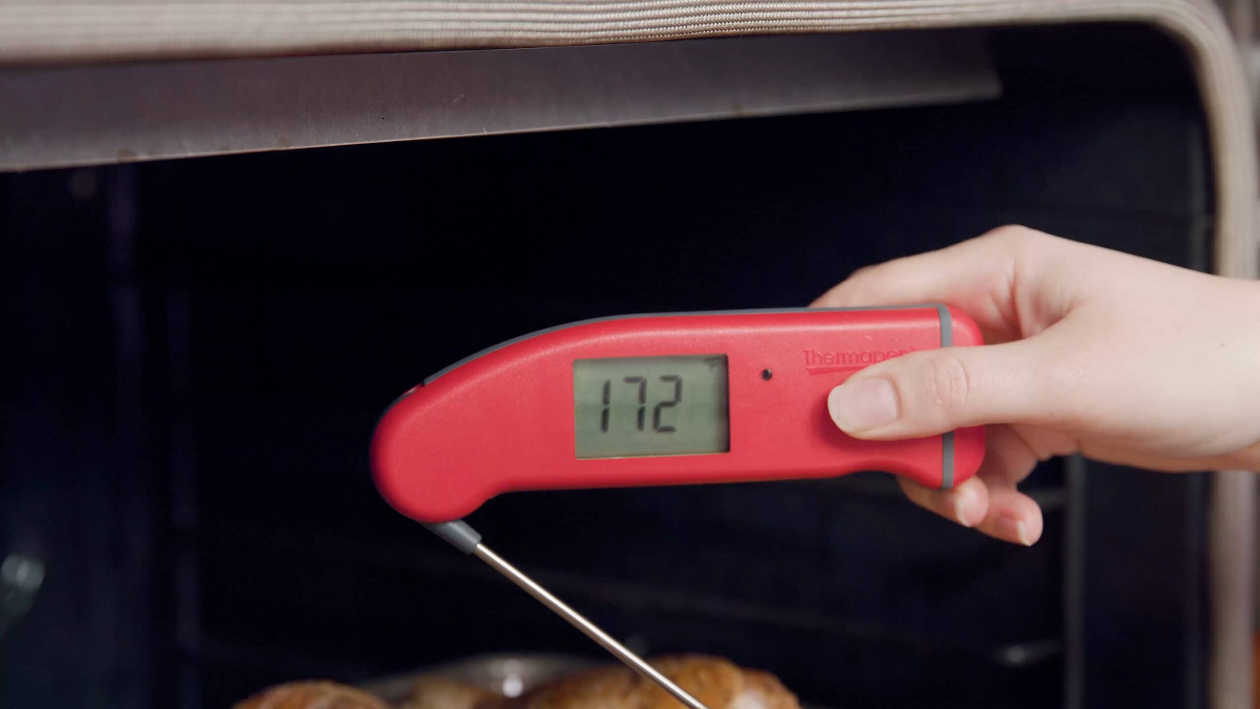 Angled view of an open oven with a digital thermometer in center view displaying 172 degrees Fahrenheit which is the ideal temperature for cooked chicken.