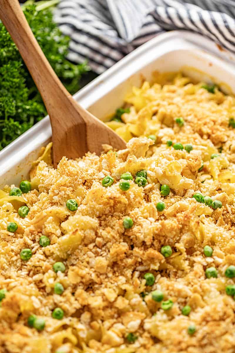 Close up of chicken casserole in a baking dish with a wooden spoon in it.