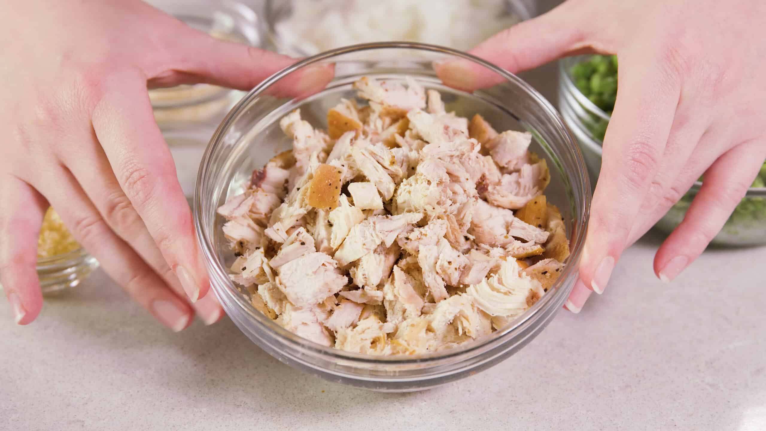 Angled view of clear glass mixing bowl filled with chopped seasoned chicken.