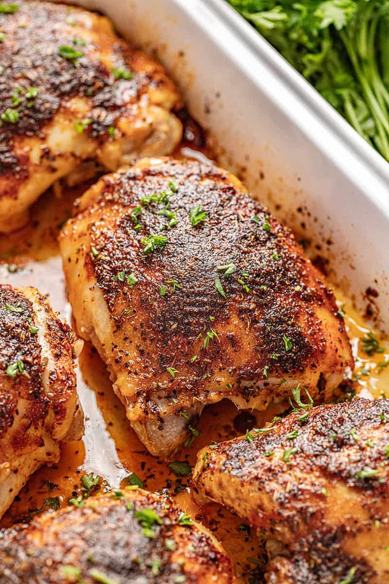 Baked Chicken Thighs in a baking dish topped with parsley and sitting in its own juices. 