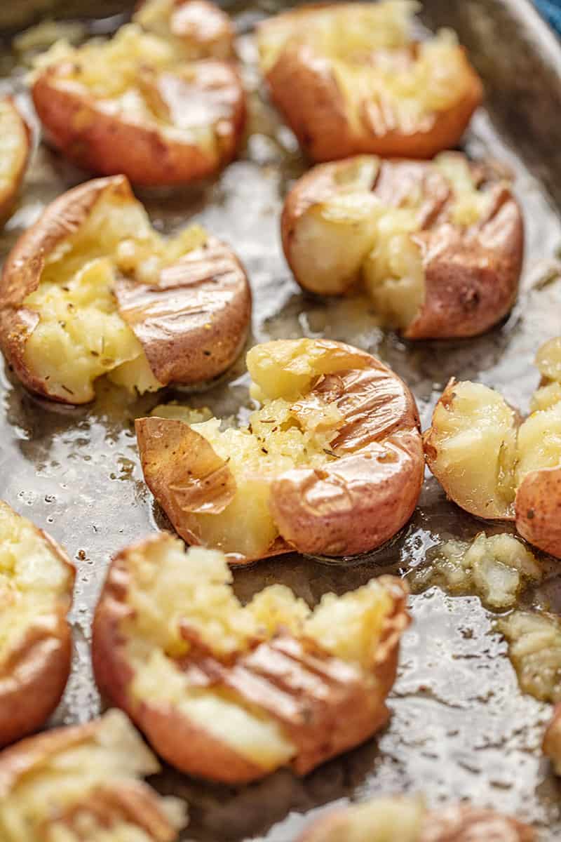 Smashed Potatoes on a baking sheet sitting in a thin layer of oil and honey.