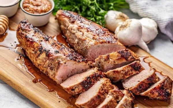 Angled view of a juicy and tender Honey Dijon Garlic Roasted Pork Tenderloin cut into slices on a wood cutting board.