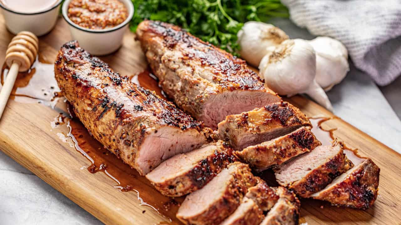 Angled view of a juicy and tender Honey Dijon Garlic Roasted Pork Tenderloin cut into slices on a wood cutting board.