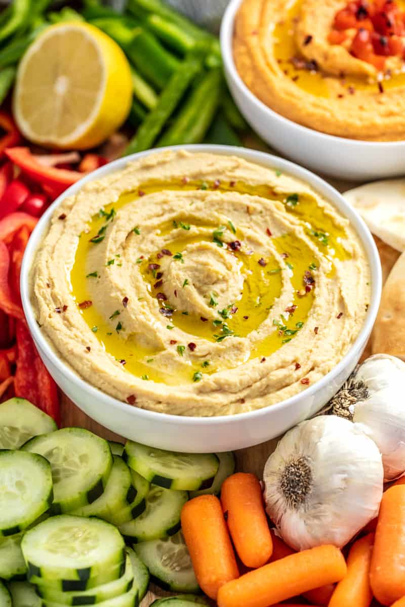 Hummus drizzled with olive oil in a white bowl surrounded by vegetables