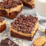 Peanut butter crunch brownies on tray with glass of milk and spoon of peanut butter