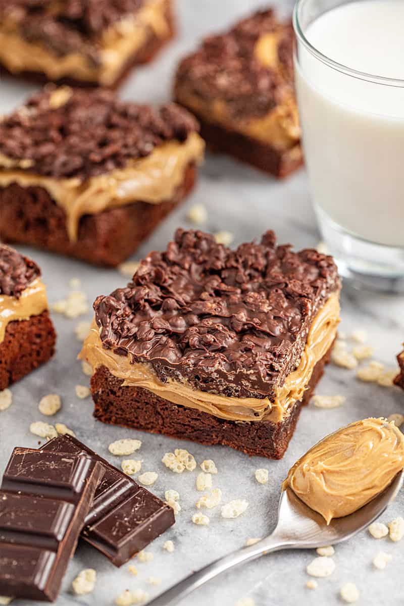 Peanut butter crunch brownies on tray with glass of milk and spoon of peanut butter