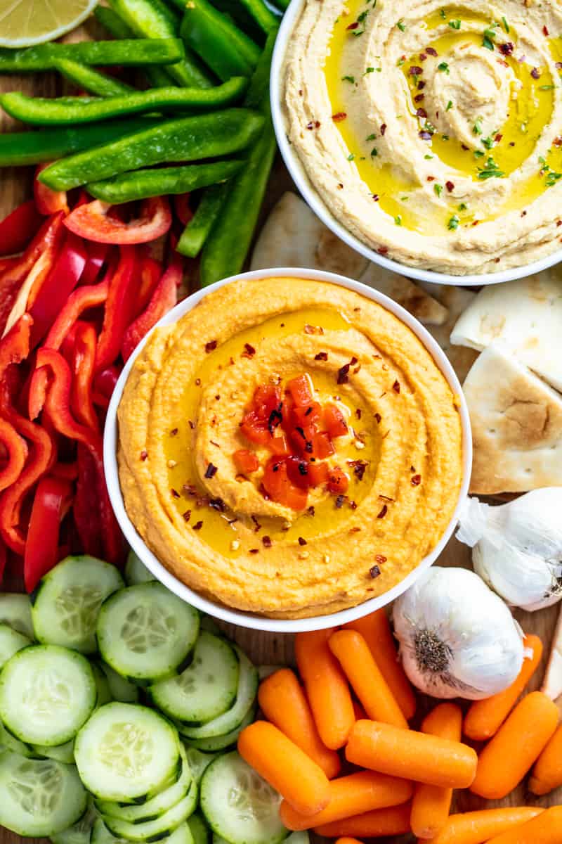Roasted Red Bell Pepper Hummus drizzled with olive oil in a white bowl surrounded by vegetables