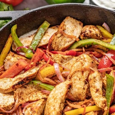 Close up view of Chicken Fajitas in a cast iron skillet with multi colored bell peppers and onion