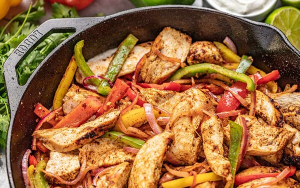 Close up view of Chicken Fajitas in a cast iron skillet with multi colored bell peppers and onion