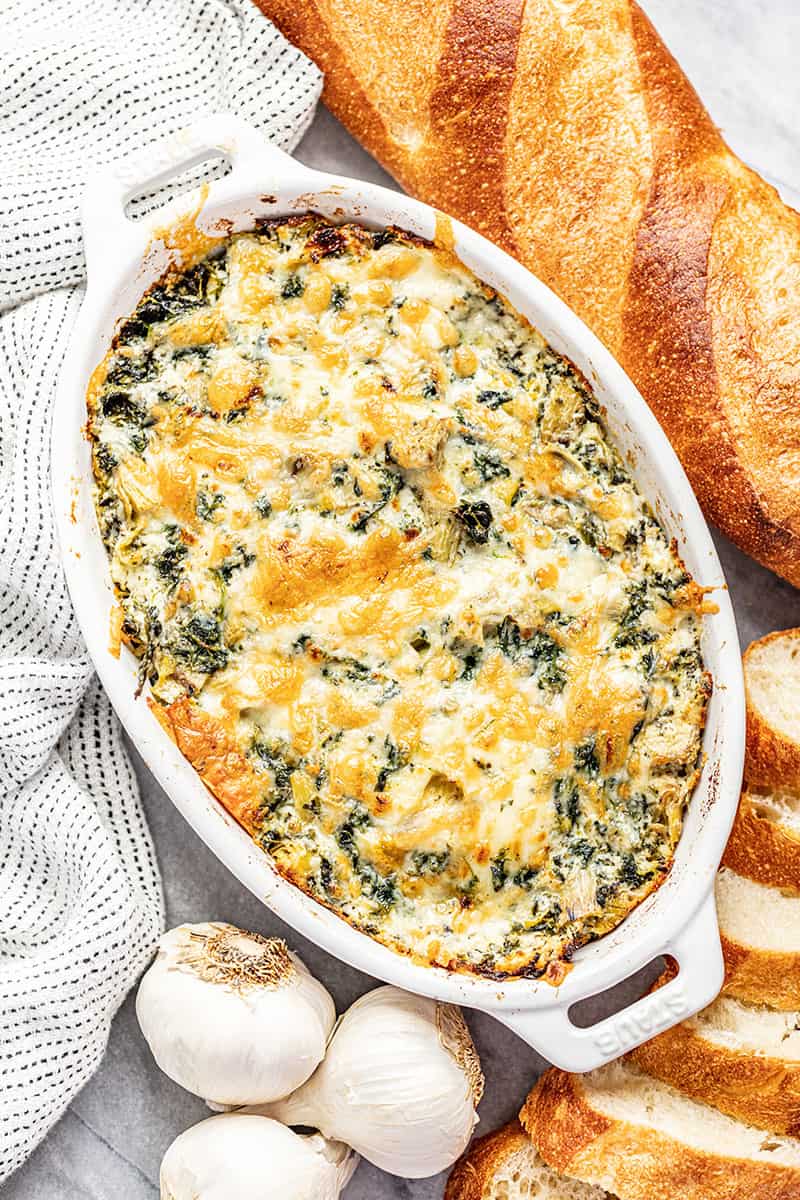 Spinach artichoke dip in white baking dish with bread in background