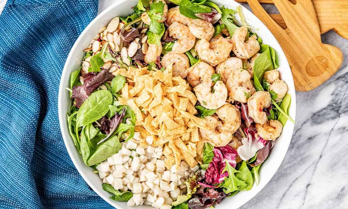 Bird's eye view of Thai Shrimp Salad topped with shrimp, crispy wonton strips, water chestnuts, slivered almonds, cilantro, and leafy greens in a white bowl.