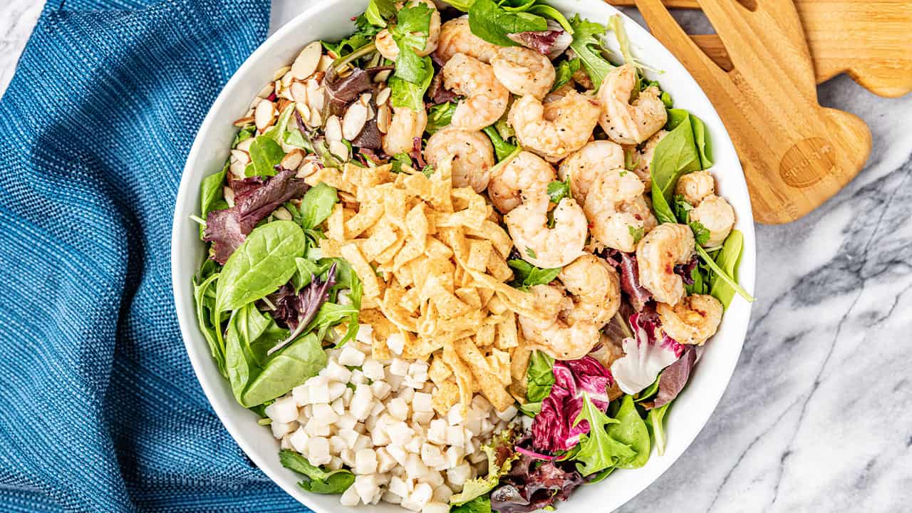 Bird's eye view of Thai Shrimp Salad topped with shrimp, crispy wonton strips, water chestnuts, slivered almonds, cilantro, and leafy greens in a white bowl.