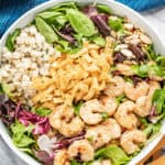 Thai Shrimp Salad topped with shrimp, crispy wonton strips, water chestnuts, slivered almonds, cilantro, and leafy greens in a white bowl