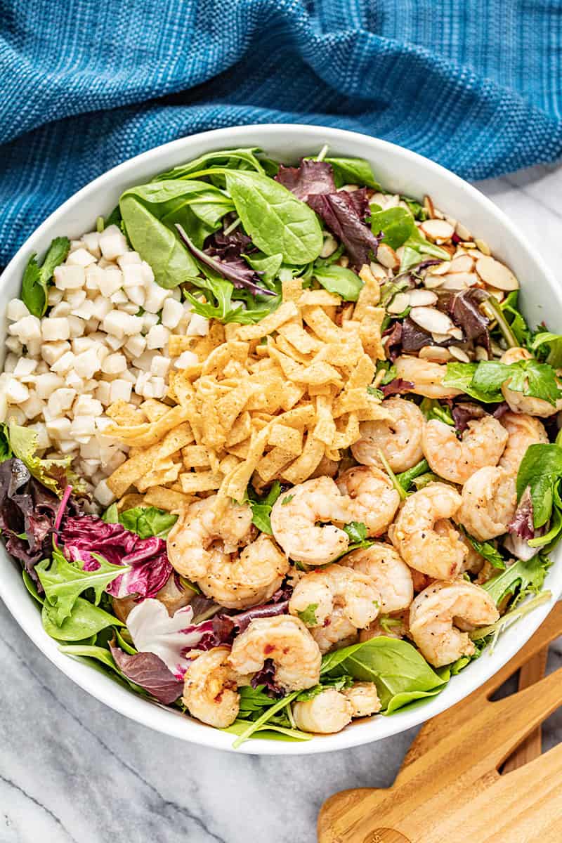 Thai Shrimp Salad topped with shrimp, crispy wonton strips, water chestnuts, slivered almonds, cilantro, and leafy greens in a white bowl