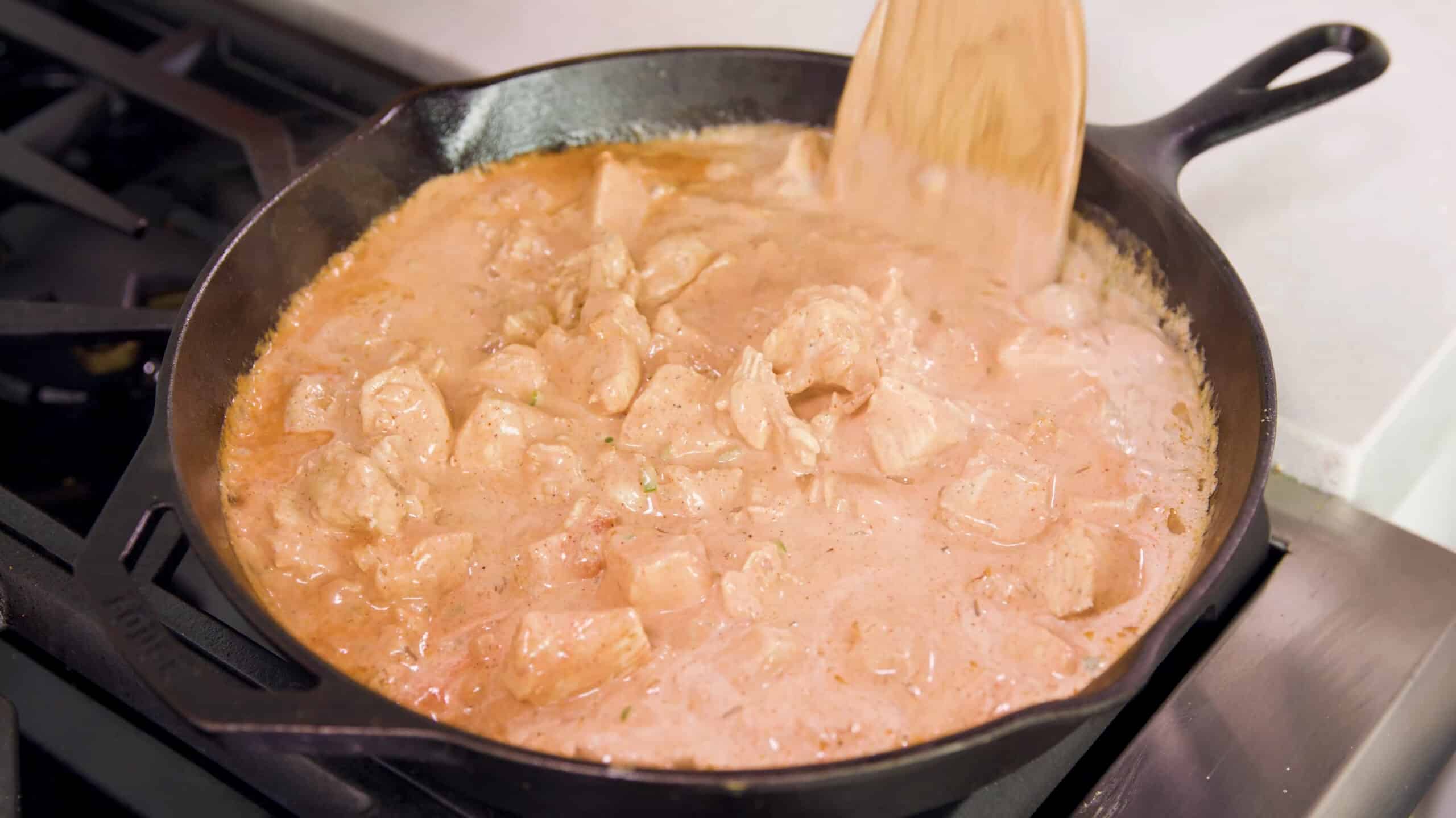 Angled view of cast iron skillet with the simmering liquid base combined with the marinaded chicken to create the Indian butter chicken dish.
