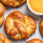 Homemade soft pretzels on a baking sheet with a cup of cheese dip