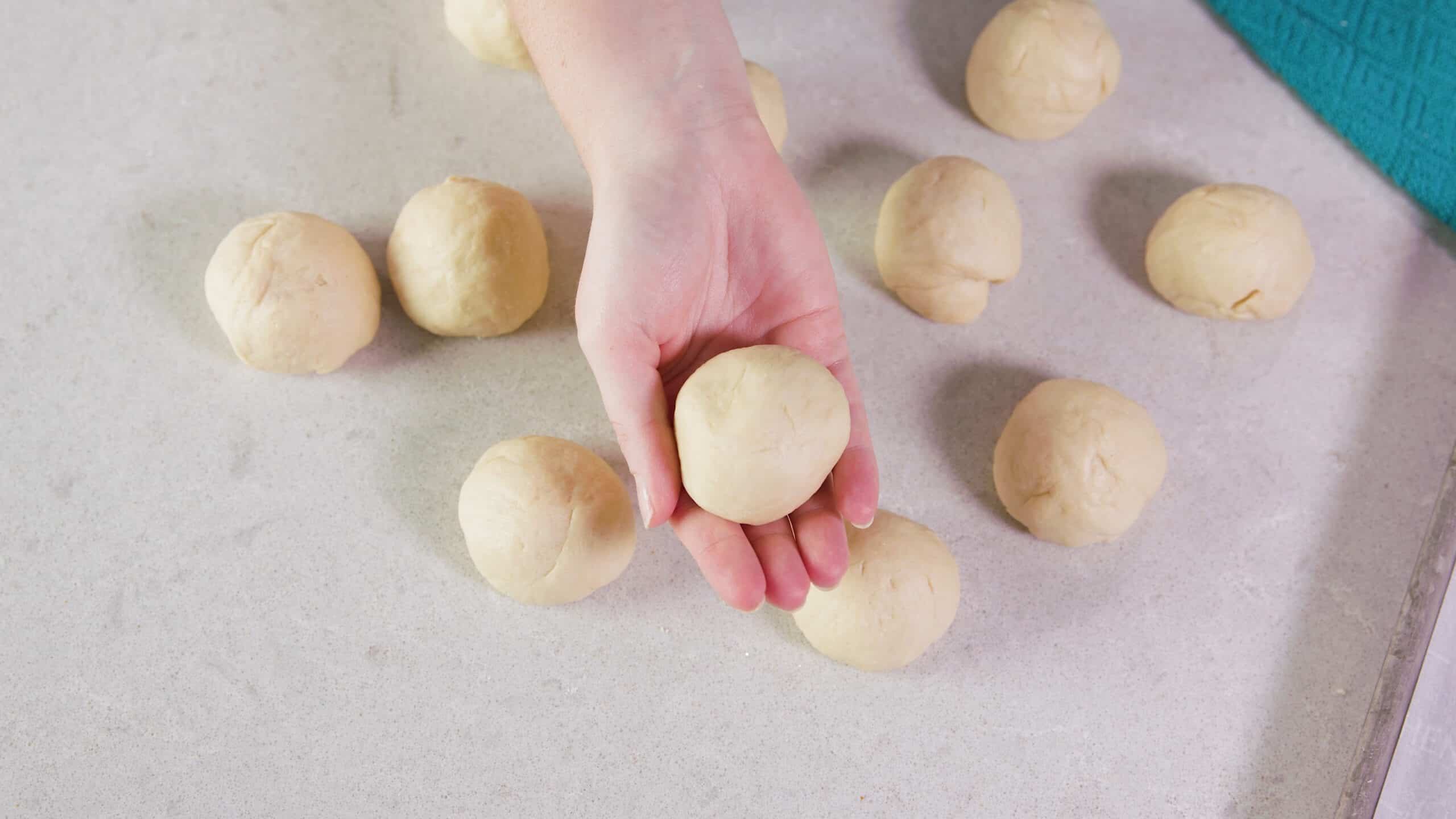 Bird's eye view of clean marble countertop with one dozen individual risen pretzel dough balls rolled and ready to form into pretzel shape.