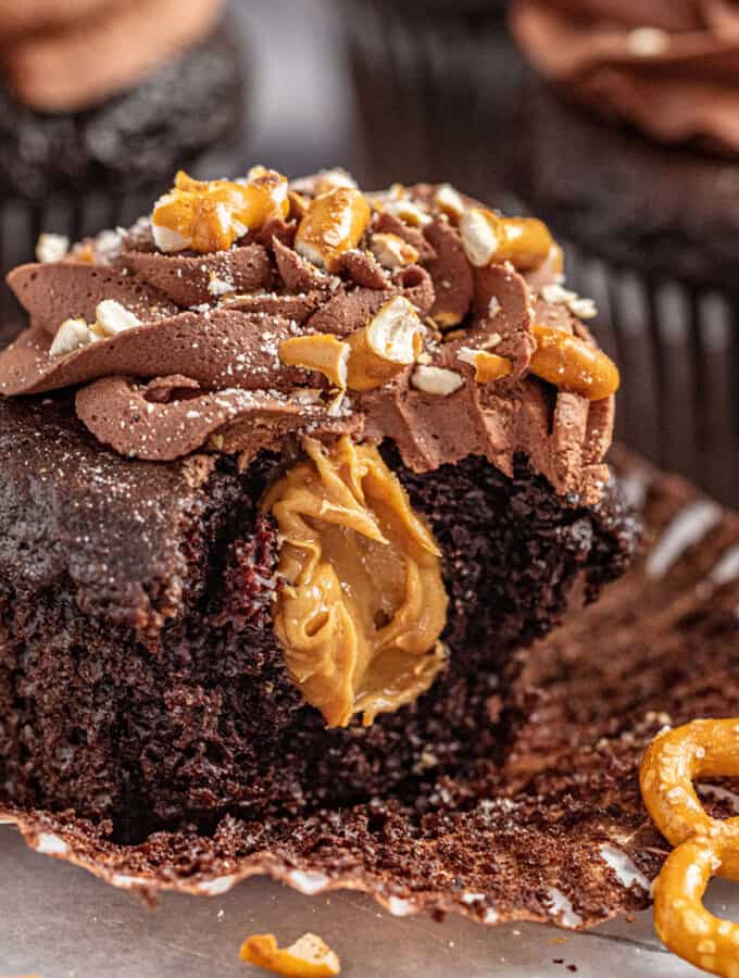 Chocolate peanut butter pretzel cupcake with bite taken out on open cupcake liner.