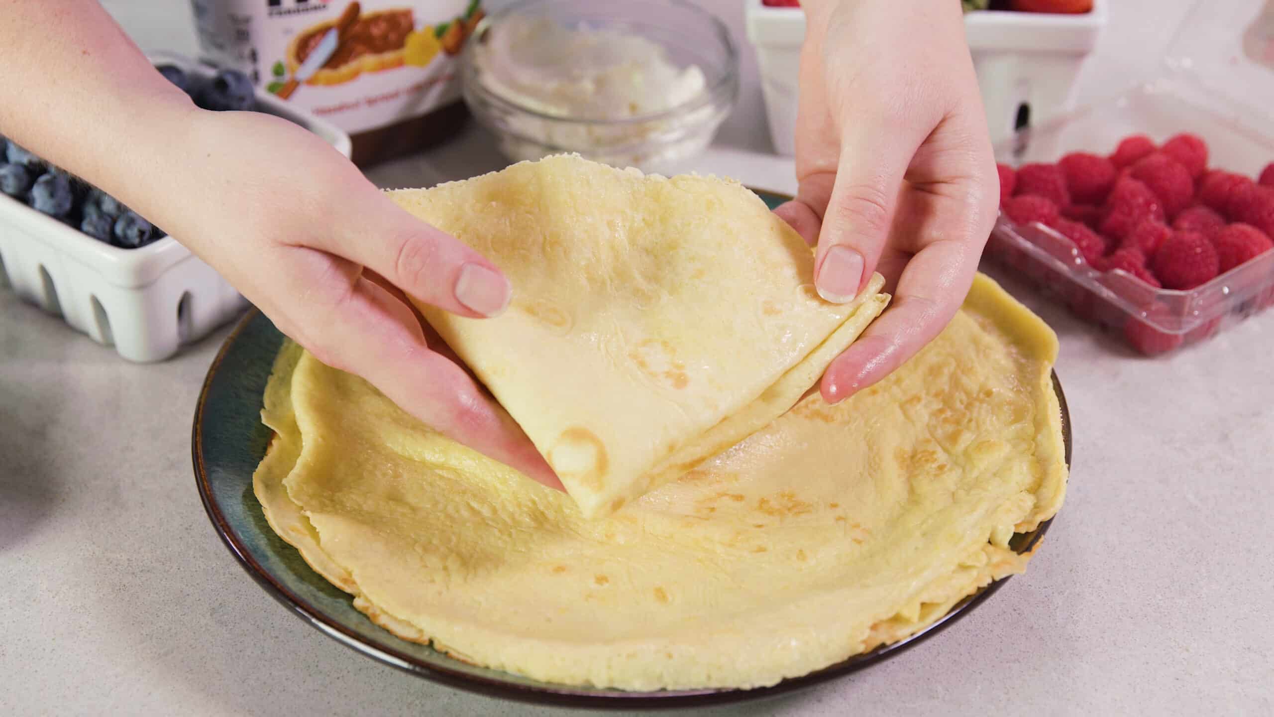 Angled view of a pair of hands holding a single crepe folded into a triangle to display one of the serving options for your crepes.