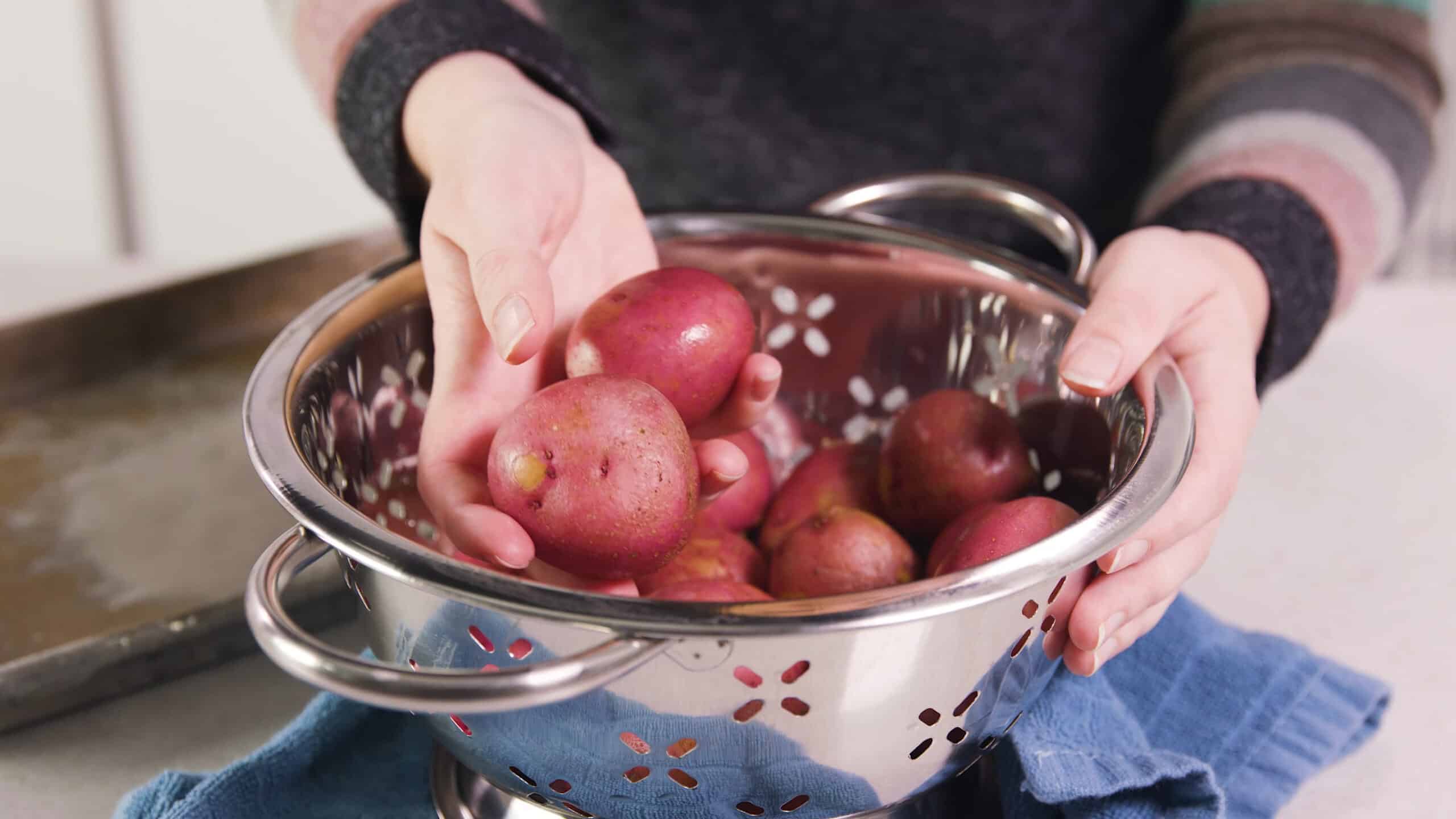 Angled view of a large metal colander filled with red potatoes.