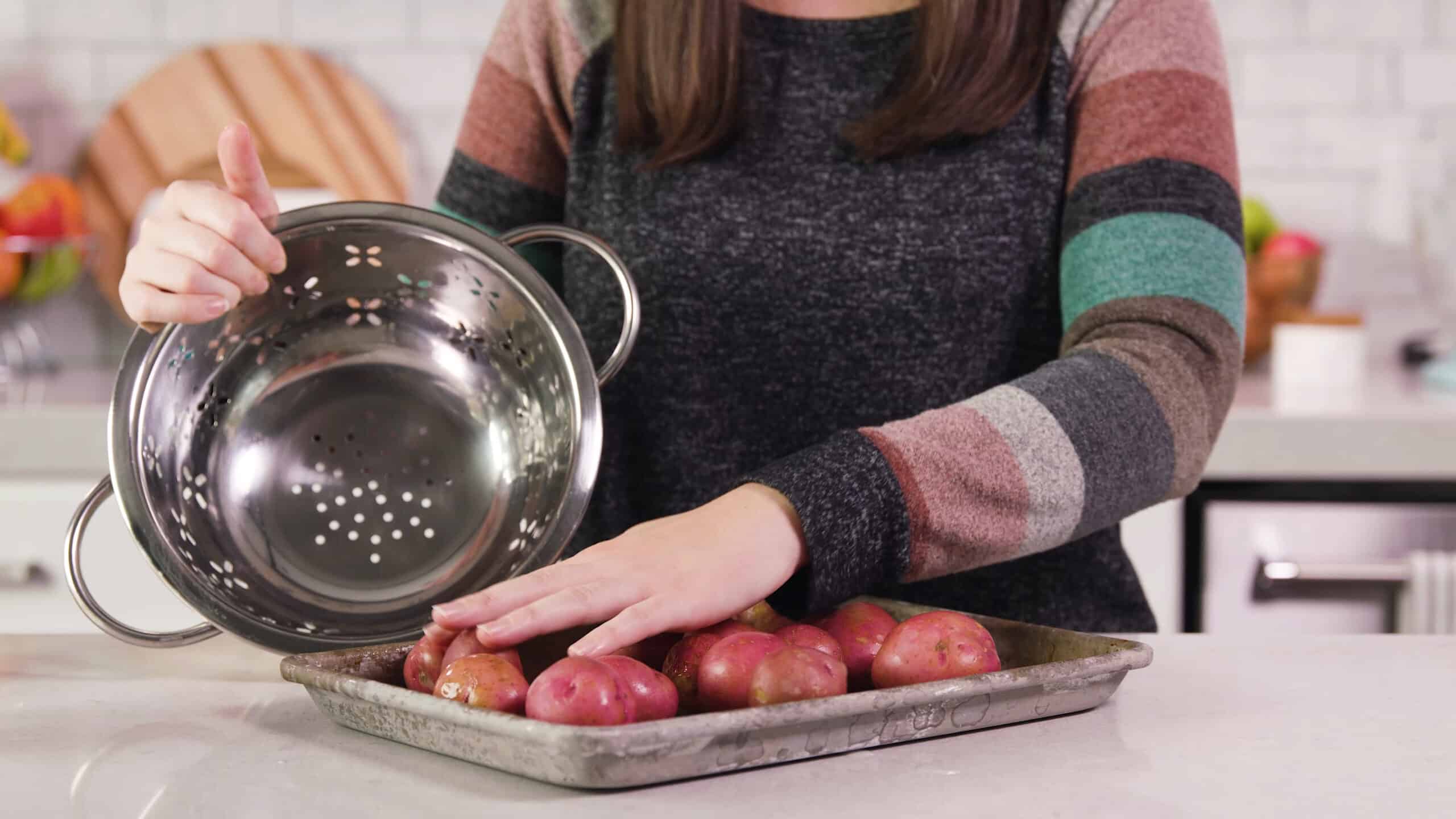 Angled view of metal baking sheet filled with about one dozen red potatoes poured from a large metal colander.