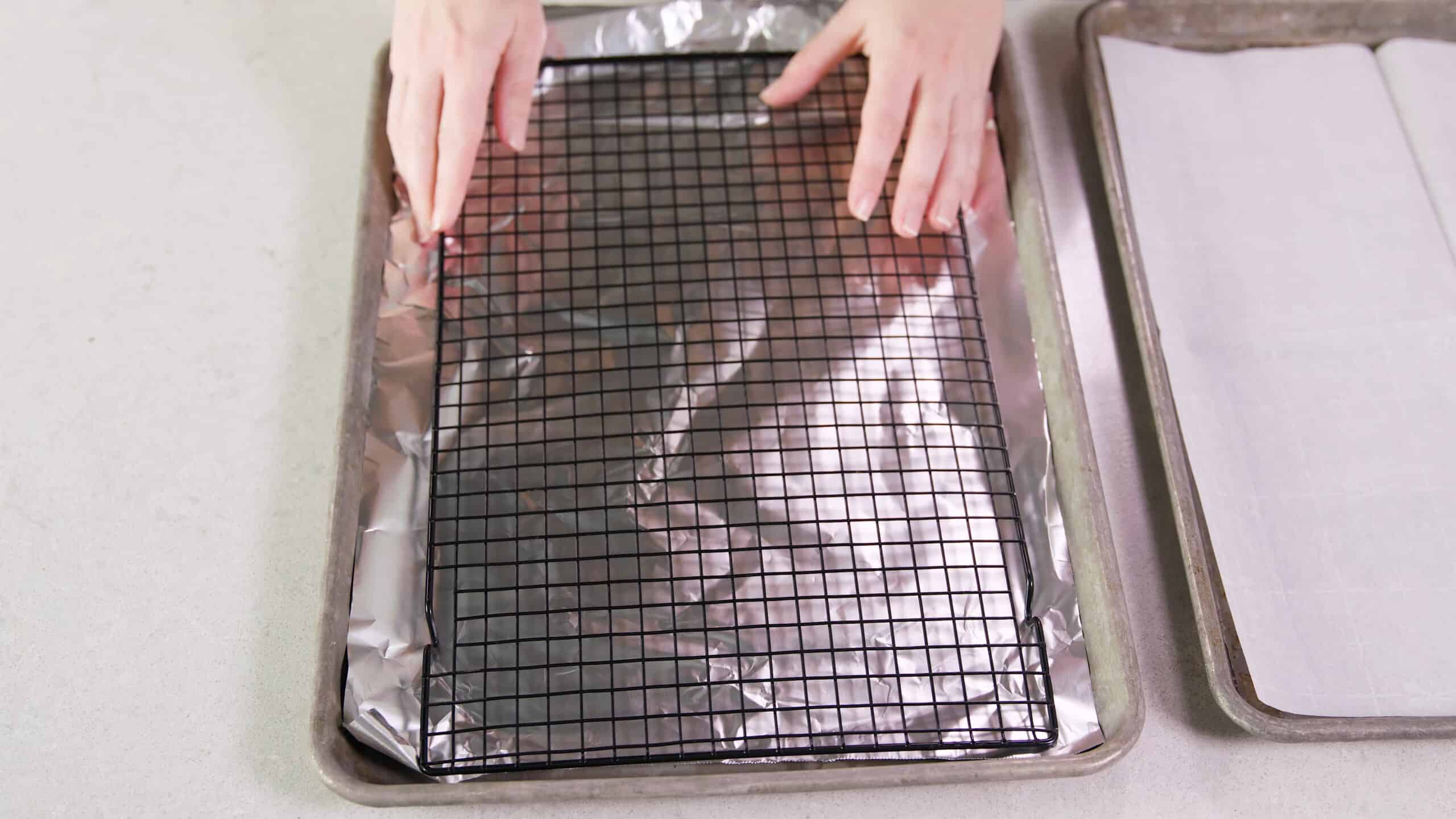 Overhead view of metal baking sheet lined with aluminum foil and a cooling rack inside and another metal baking sheet lined with parchment paper to the side.