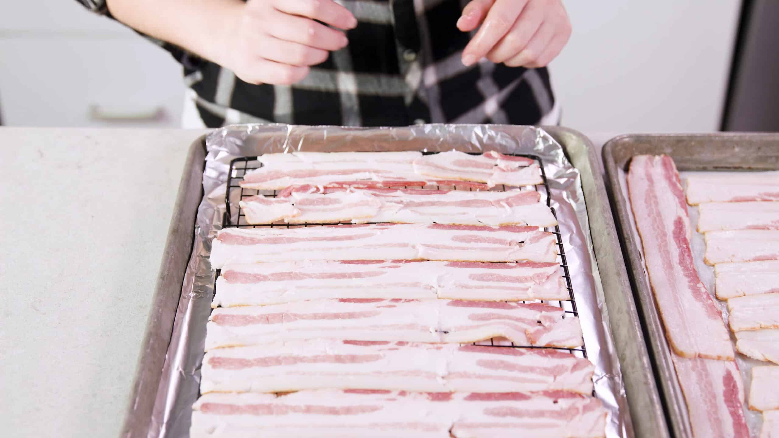 Angled view of metal baking sheet lined with aluminum foil and a cooling rack inside lined with strips of bacon.