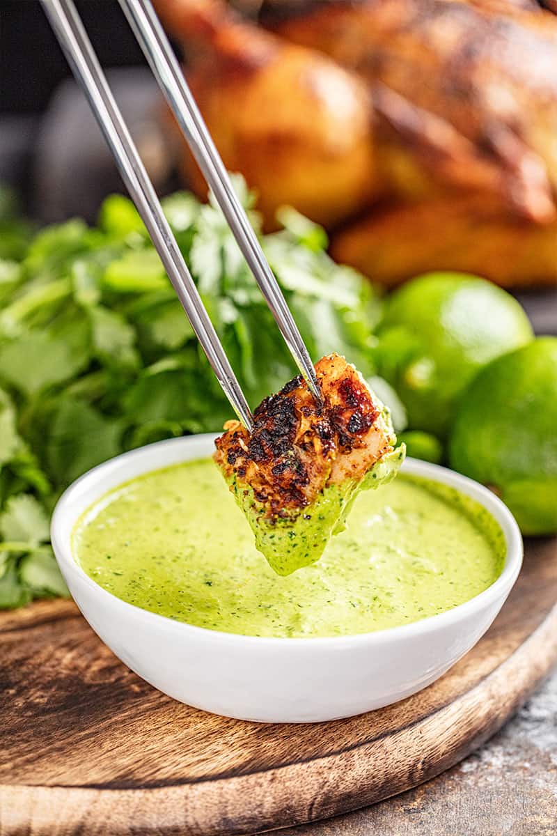 A piece of oven roasted Peruvian chicken being dipped into green sauce