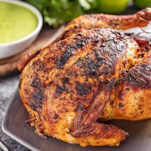 Oven roasted Peruvian chicken on a platter with a side of green dipping sauce