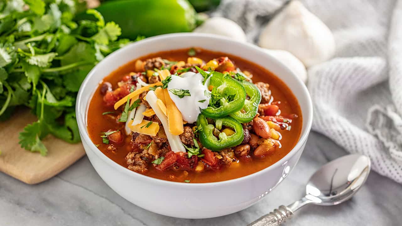 Taco soup with jalapeños sour cream and cheese on top in a white bowl