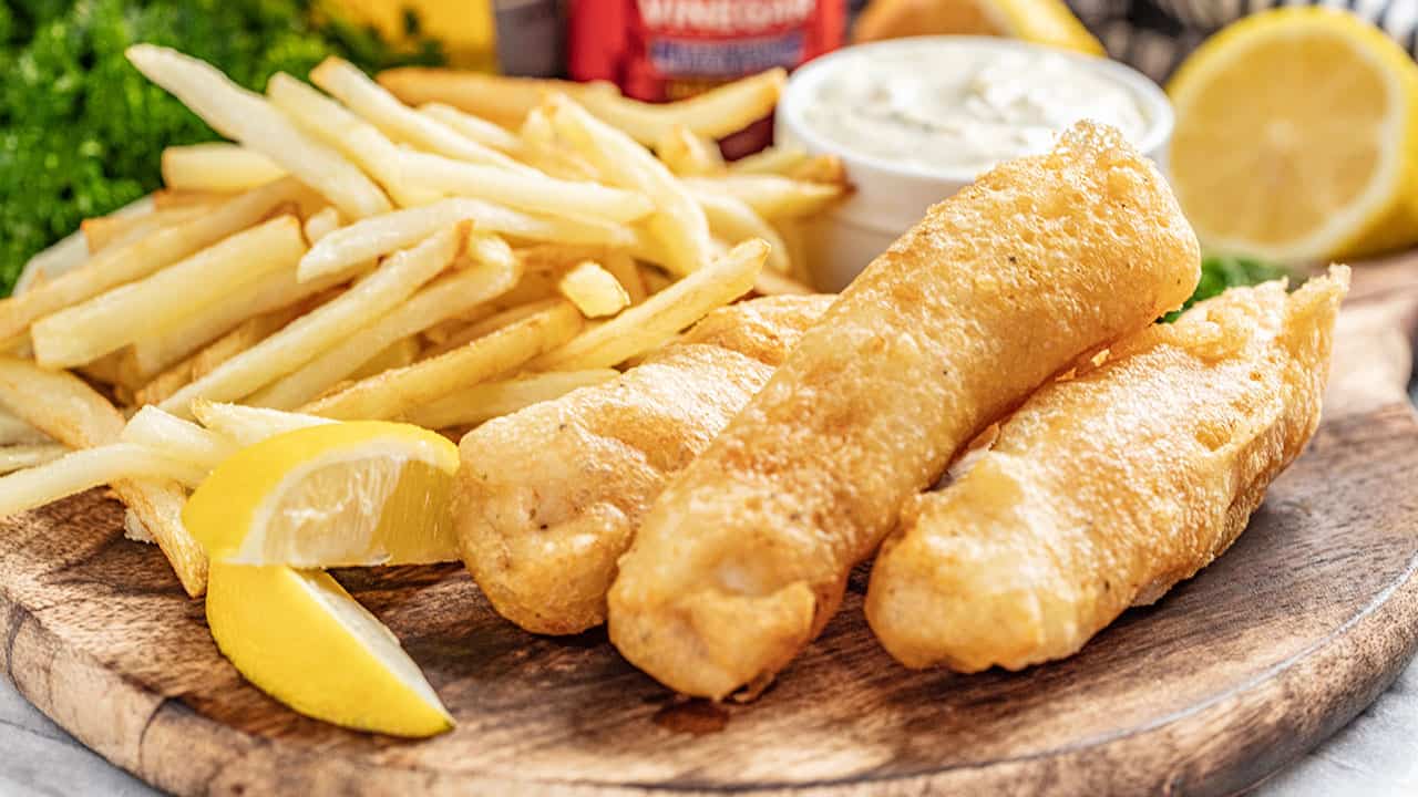 Beer battered fish and chips on serving plate with lemon wedges