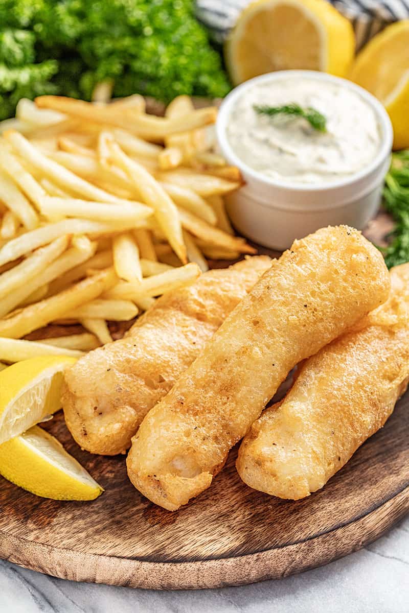 Beer battered fish and chips on serving plate with lemon wedges and tartar sauce