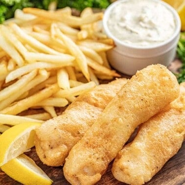 Beer battered fish and chips on serving plate with tartar sauce and lemon wedges