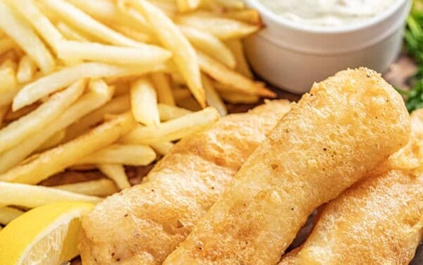 Beer battered fish and chips on serving plate with tartar sauce and lemon wedges