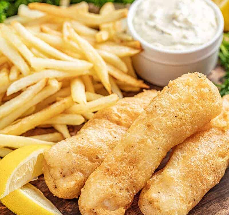Beer battered fish and chips on serving plate with tartar sauce and lemon wedges