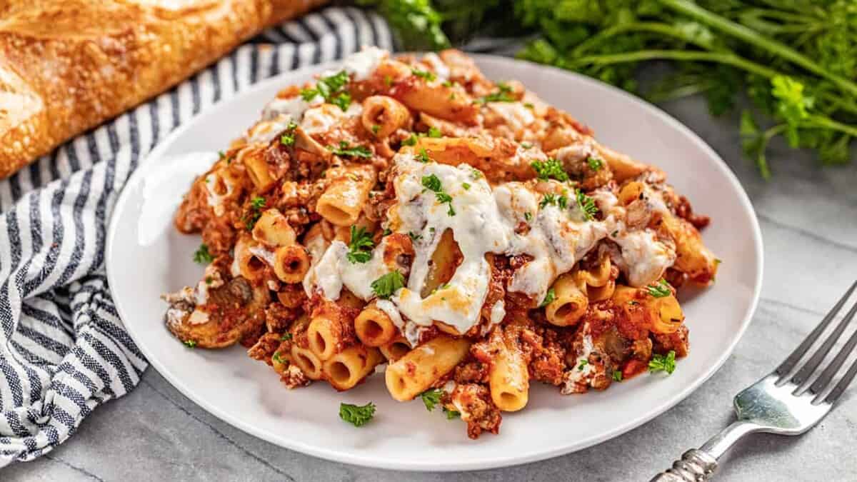 A large serving of baked ziti sprinkled with parsley on a white plate