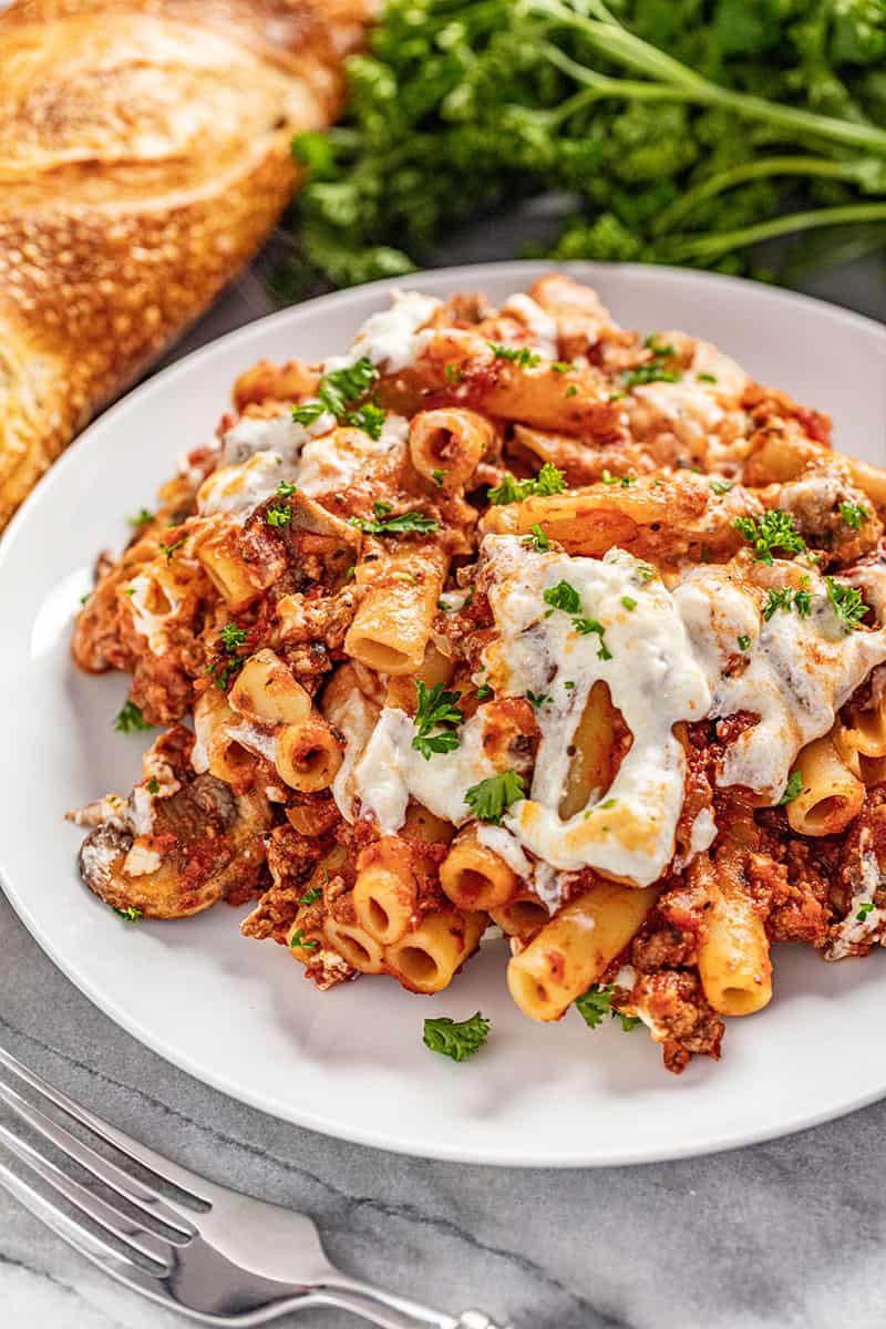 A serving of baked ziti sprinkled with parsley on a white plate