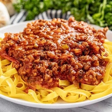 Bolognese sauce on white plate on bed of noodles