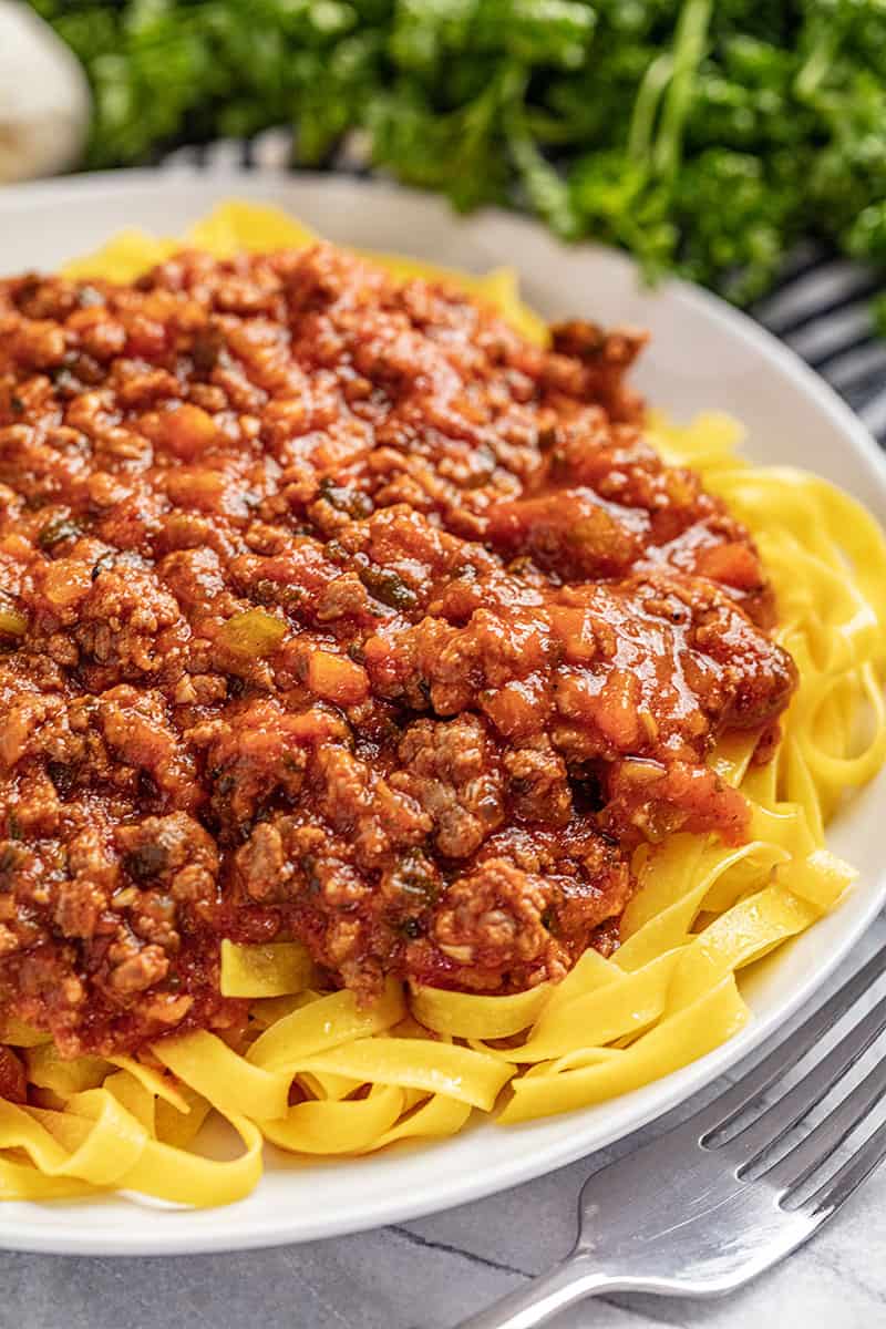 Bolognese sauce on white plate on bed of noodles