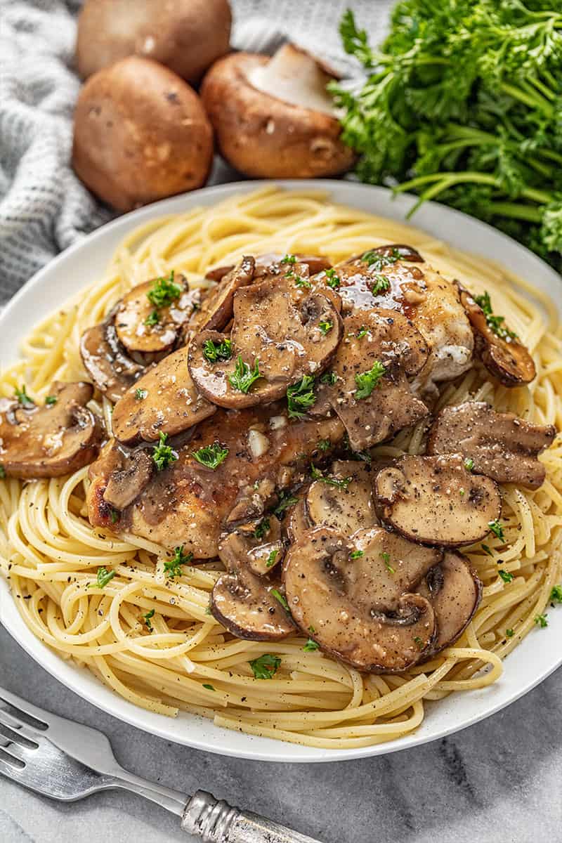 Chicken marsala on a white plate on bed of spaghetti noodles