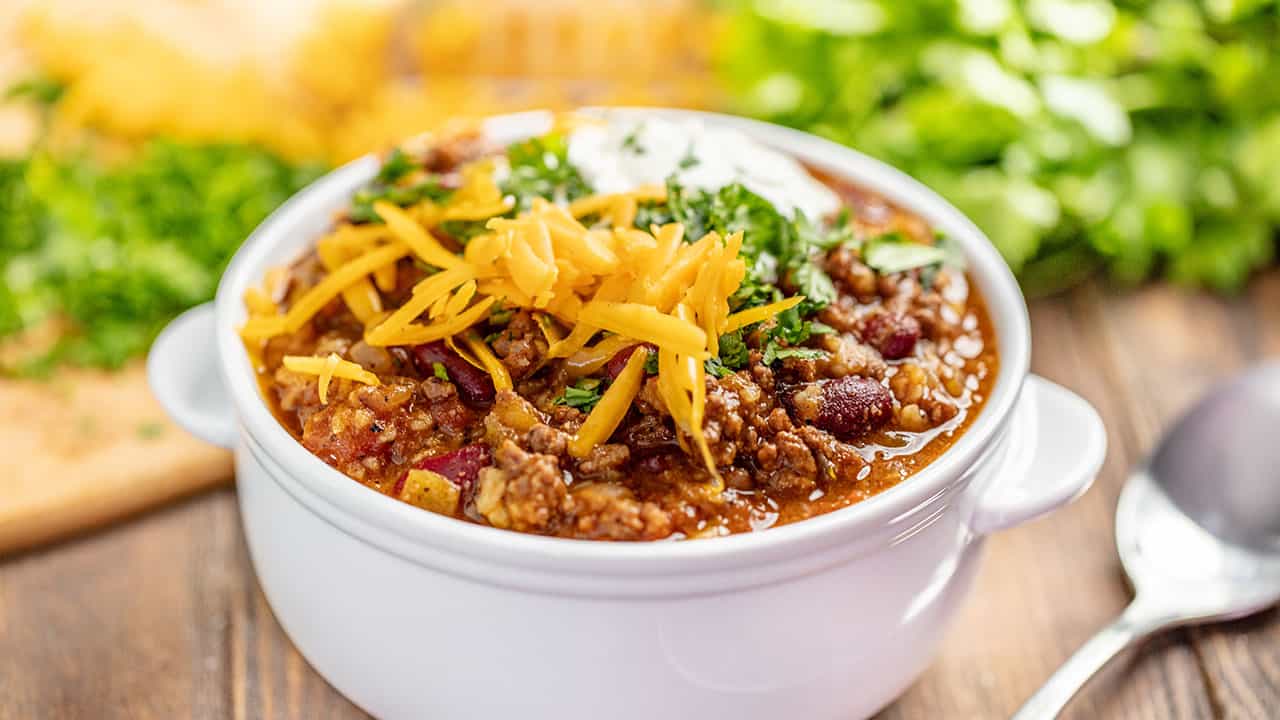 A cup of chili with cheese on top in white ceramic bowl