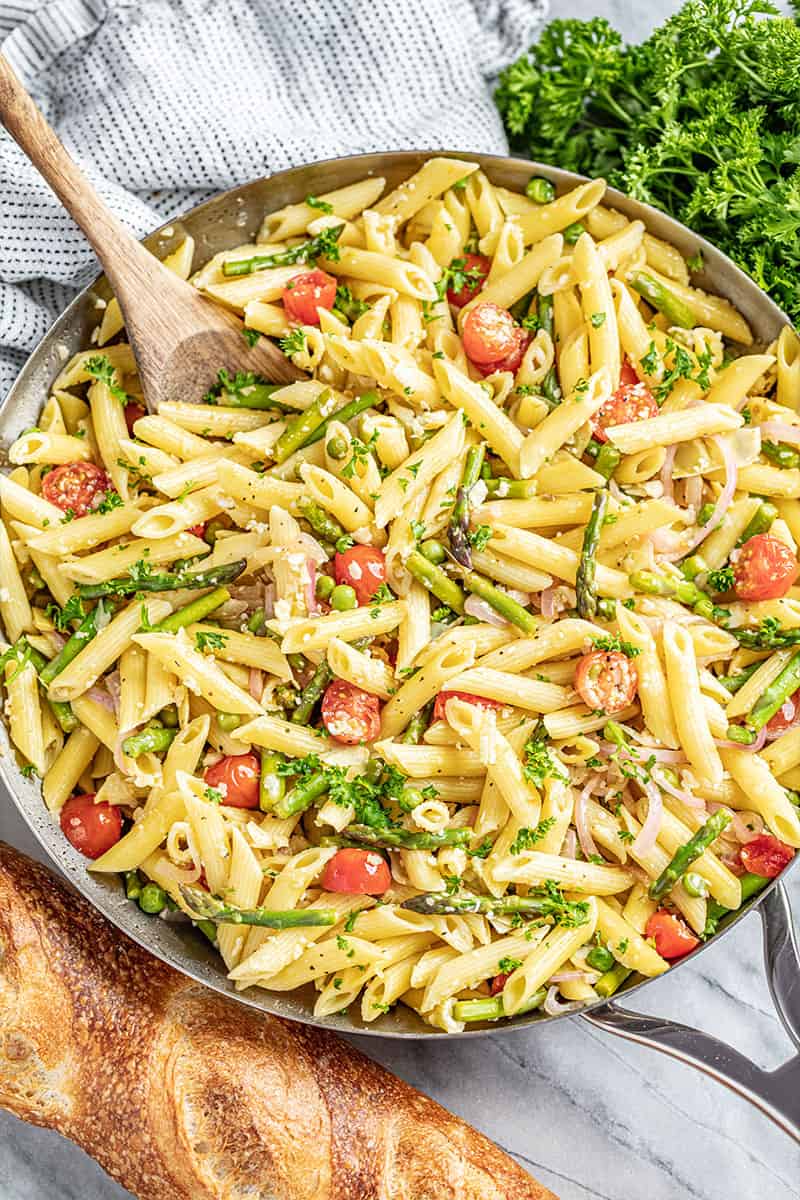 Creamy pasta primavera in skillet with wooden spoon