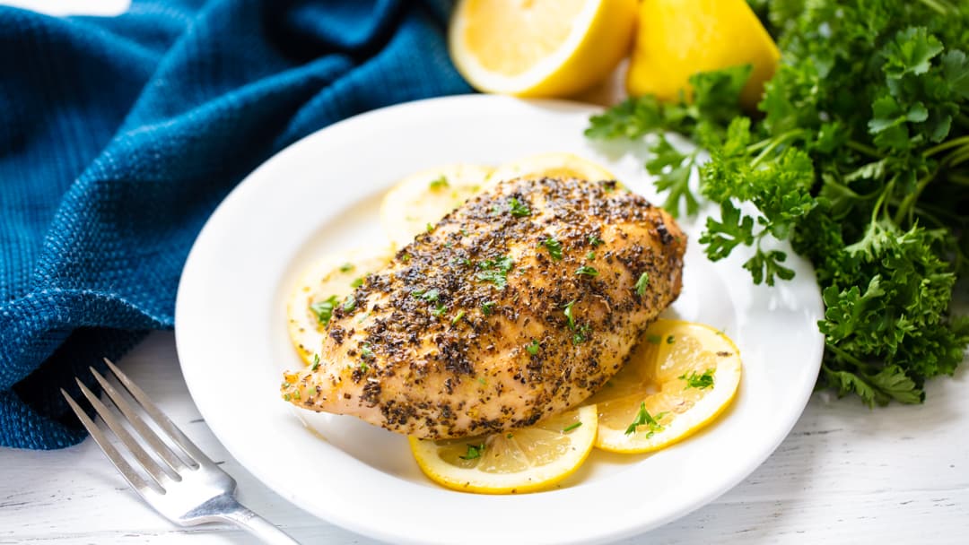 Pechuga de pollo a la pimienta de limón sobre rodajas de limón en un plato blanco