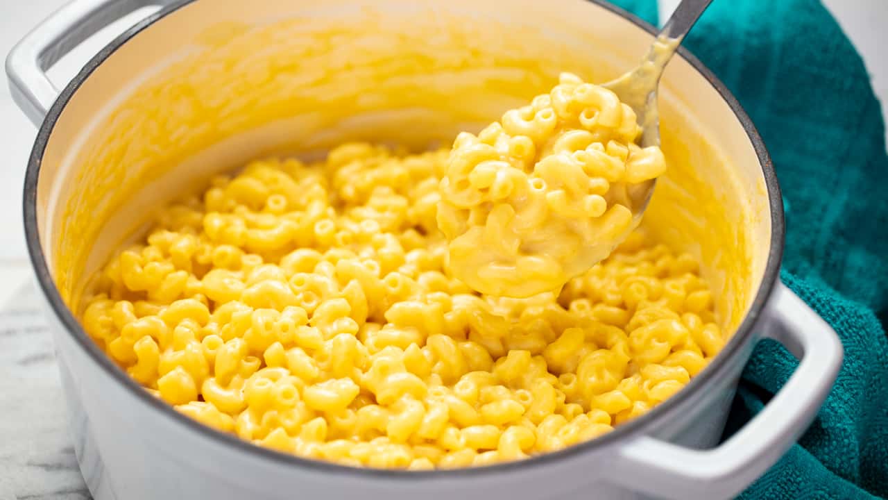 Mac and cheese in a white stock pot with a spoon