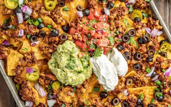 Nachos on a baking sheet with salsa and green onions on the side