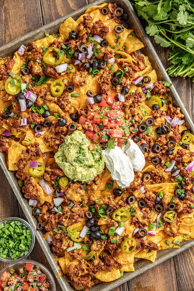 Nachos on a baking sheet with salsa and green onions on the side