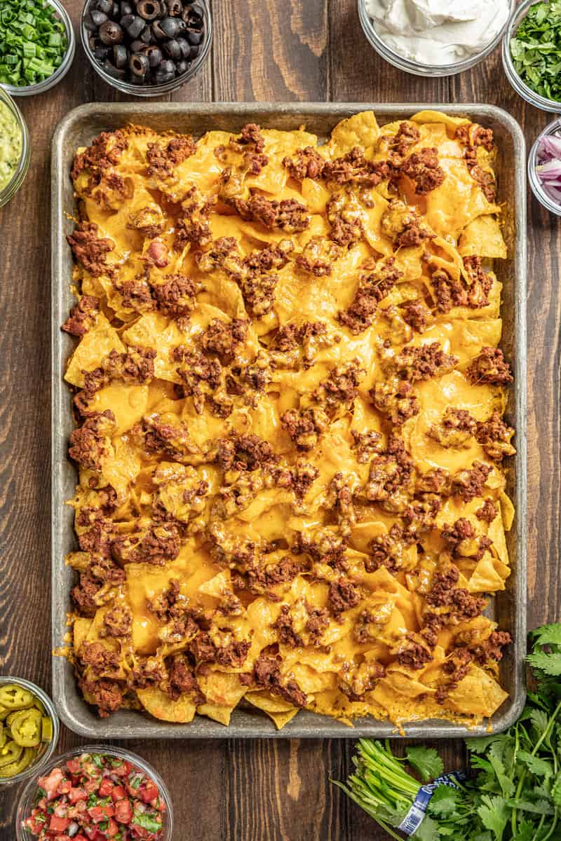 Nachos on a baking sheet surrounded by toppings