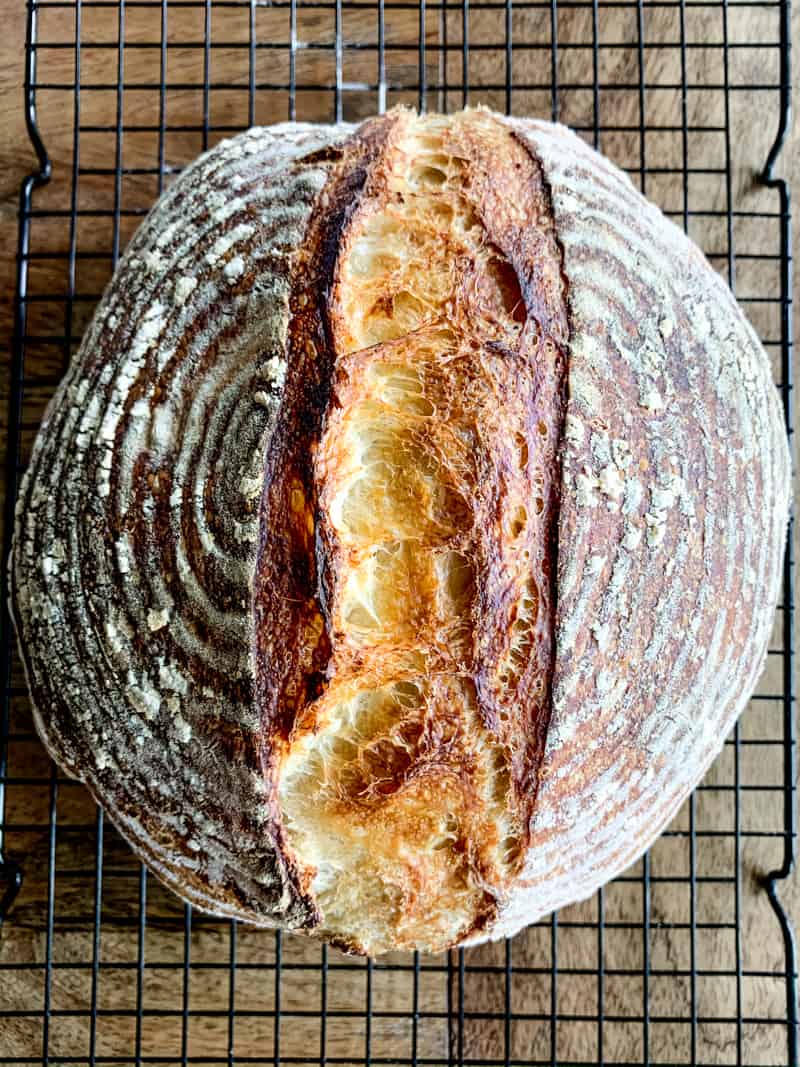 Baked loaf of sourdough bread on a black wire cooling rack